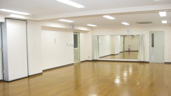 白い壁紙で大きな鏡が壁面に設置されているフローリングの床の研修室の写真