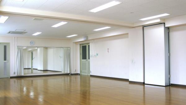 白い壁紙で大きな鏡が壁面に設置されているフローリングの床の研修室を斜めから映した写真