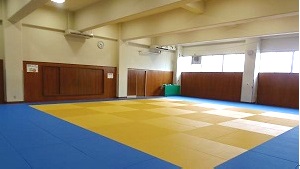 白と茶色の壁紙に外周に青いマットが敷かれ中央に畳の敷かれている柔道場の写真
