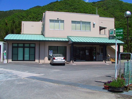 薄い緑色の屋根付きの入口がある西栗栖コミュニティセンターの二階建ての建物を写した写真