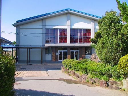 二階に大きな窓があり水色の三角屋根をした誉田小学校の体育館を正面から写した写真