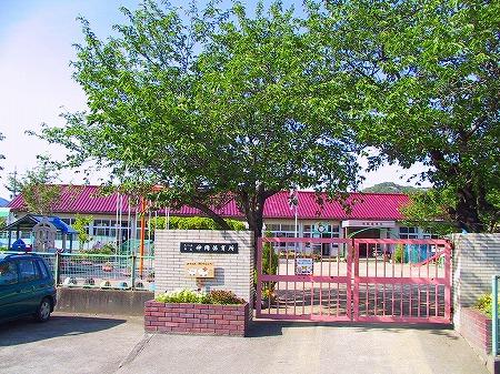 ピンクの門の奥に緑の木々が生え、その奥に建つピンクの屋根の神岡保育所の建物を正面から写した写真