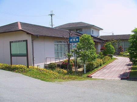 入口に避難所の案内板があり、奥に続く小さな道が設けられた外壁がピンクの河内コミュニティセンターの建物を写した写真