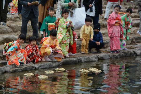 着物を着た子供たちが桟俵にのせた流しびなを揖保川へ流している様子を撮影した写真