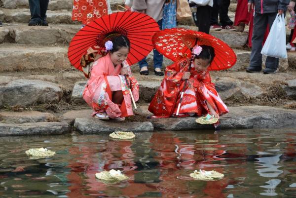 ピンクの着物に赤い和傘を差した2人の女の子が流しびなを揖保川へ流している写真