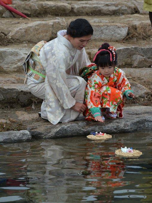 着物を着た親子が桟俵にのせた流しびなを揖保川へ流している写真