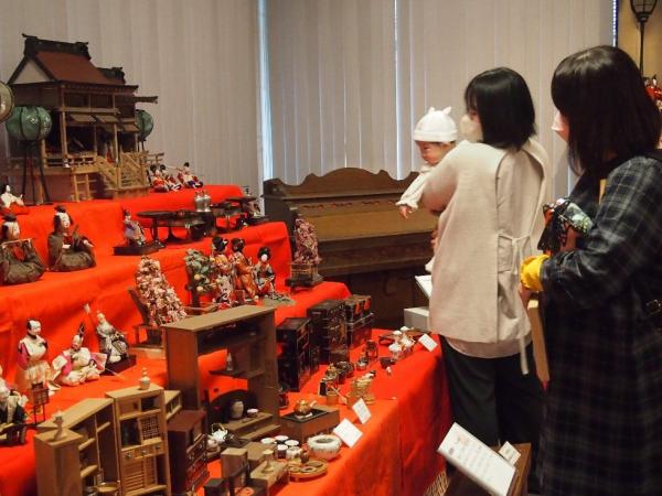 室内に展示された雛人形をお母さんに抱っこされながら見ている乳幼児の写真