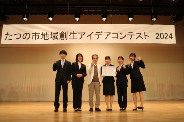 最優秀賞を受賞した同志社大学政策アイデアチームの皆さんが、舞台の上に立ち賞状を持って記念写真を撮っている写真
