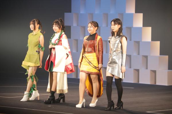 ワンピースや着物を洋服のように身にまとった4人の女性がライトのあたる舞台の上に立っている写真