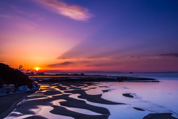 太陽が沈んでいく夕焼けの手前に広がる干潟が幻想的な新舞子浜の写真